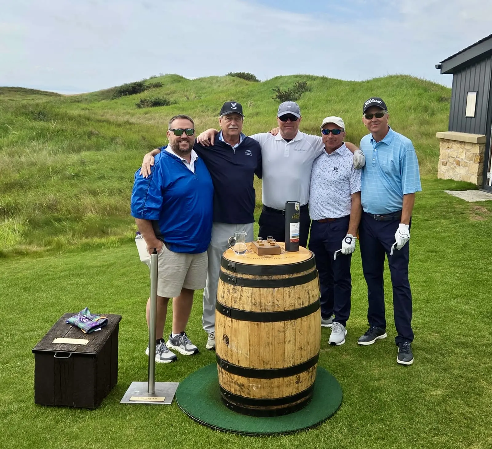 Five golfers standing by wooden barrel.