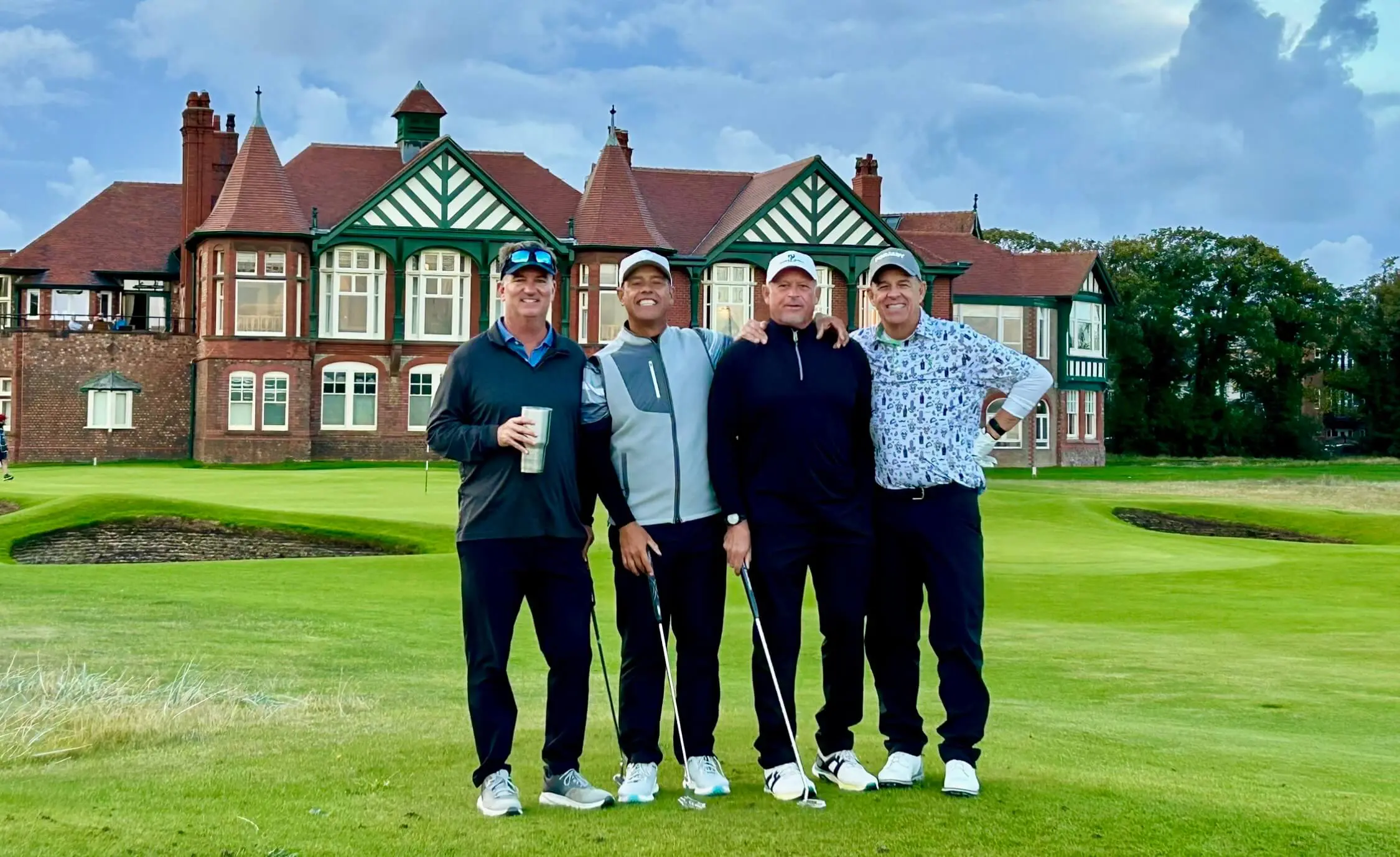 Four golfers posing in front of clubhouse.