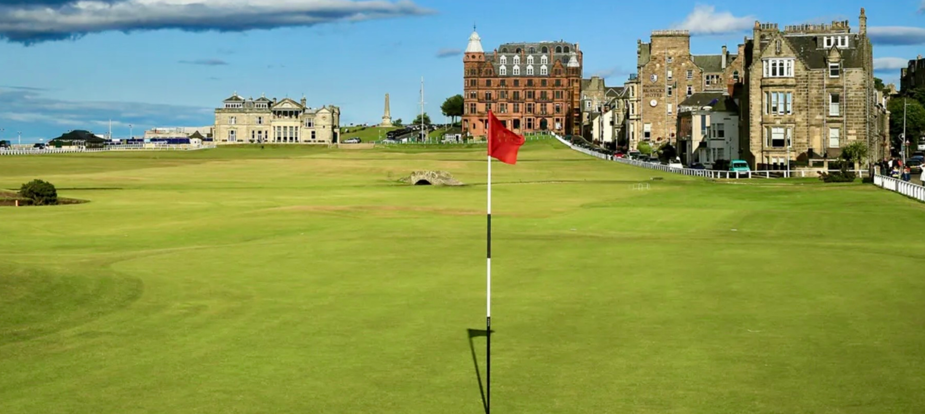 Golf course with flag and historic buildings.